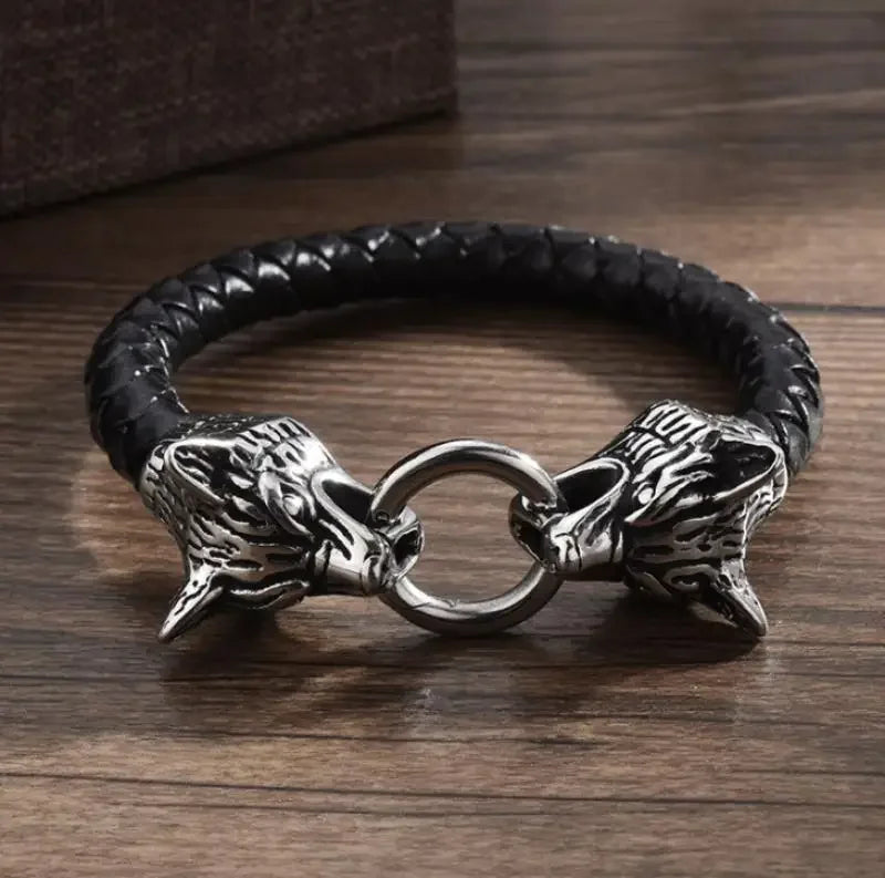 Black braided leather bracelet with silver wolf head clasps on a wooden surface