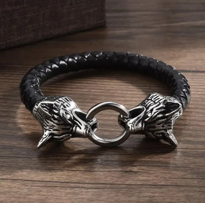 Black braided leather bracelet with silver wolf head clasps on a wooden surface