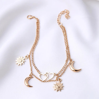 Gold bracelet with moon, sun, and heart charms on a white background