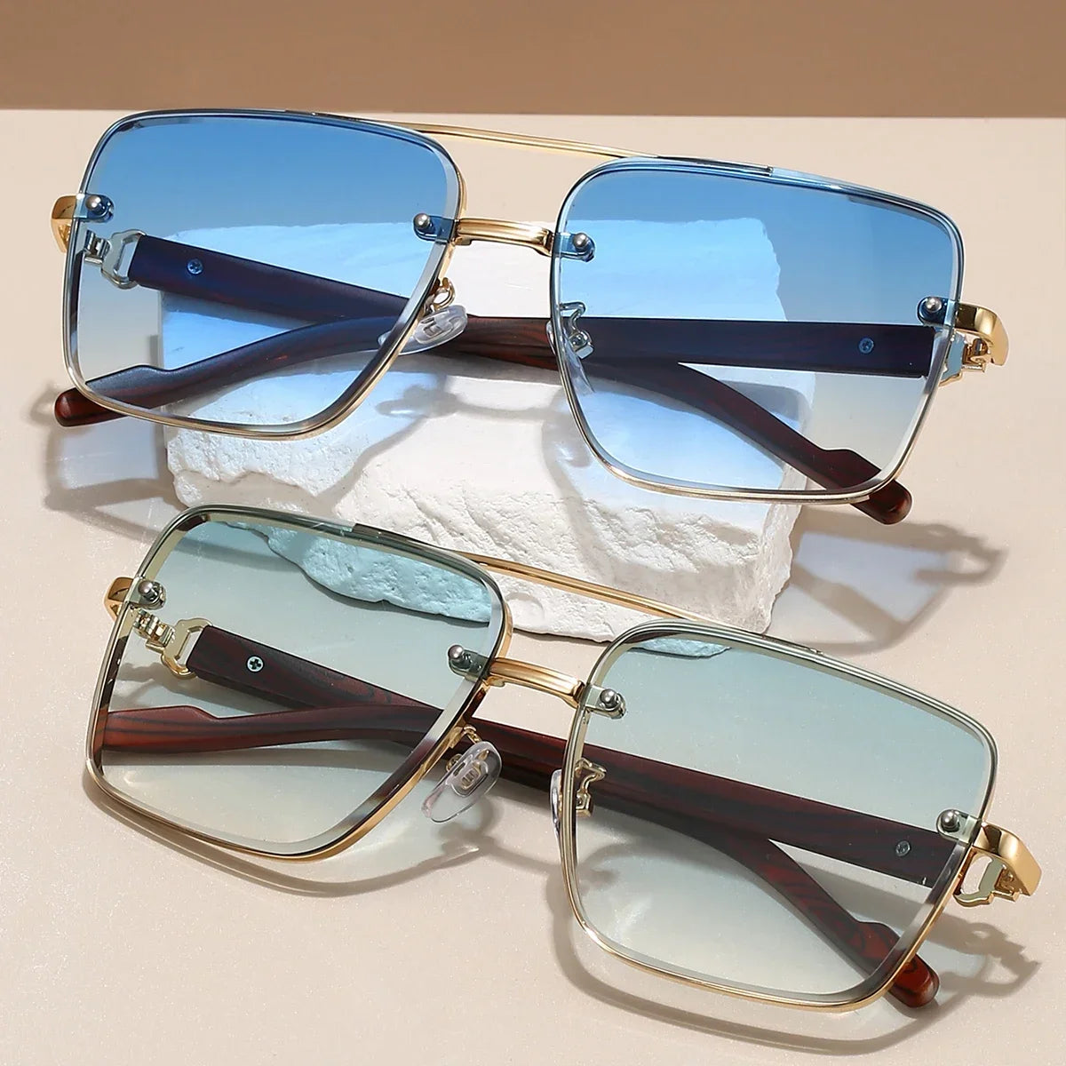 Pair of sunglasses with gold frames and blue-tinted lenses on a beige surface.