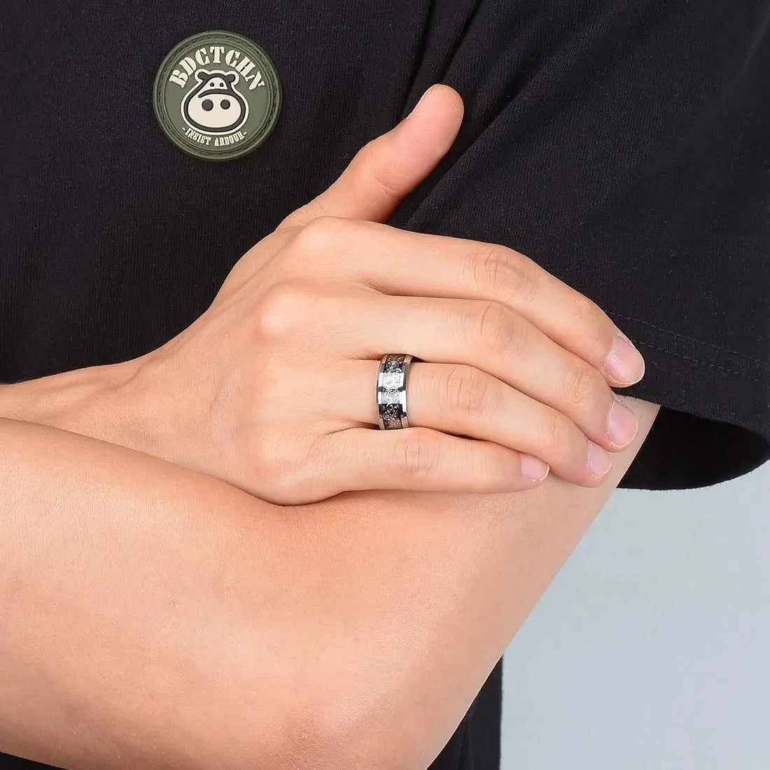 Close-up of a hand wearing a silver ring with a black shirt featuring a logo in the background