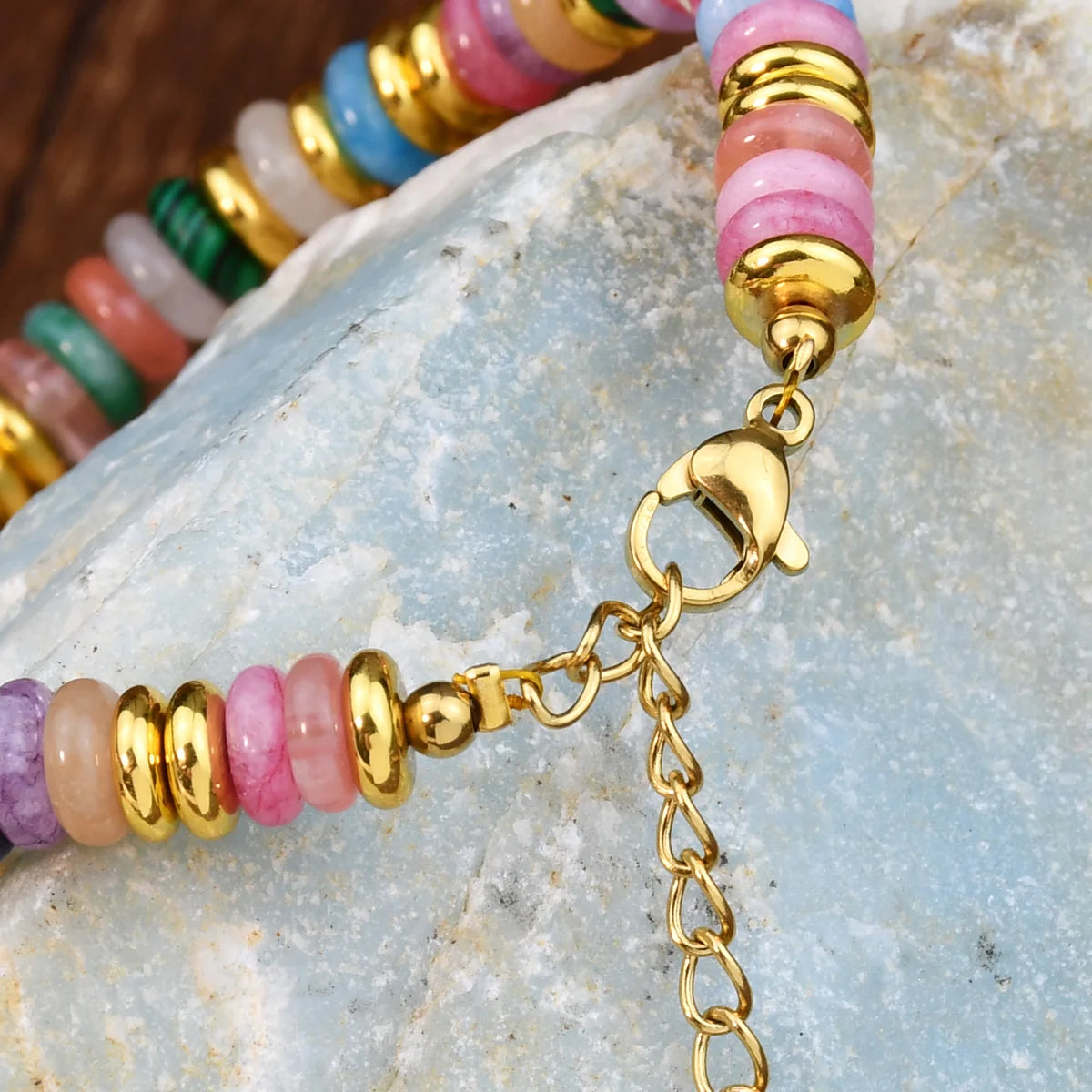 Colorful beaded bracelet with gold chain on a stone surface