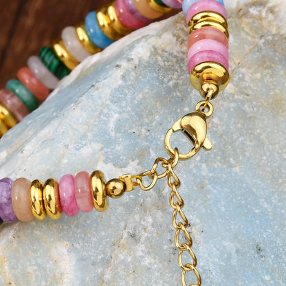 Colorful beaded bracelet with gold chain on a stone surface