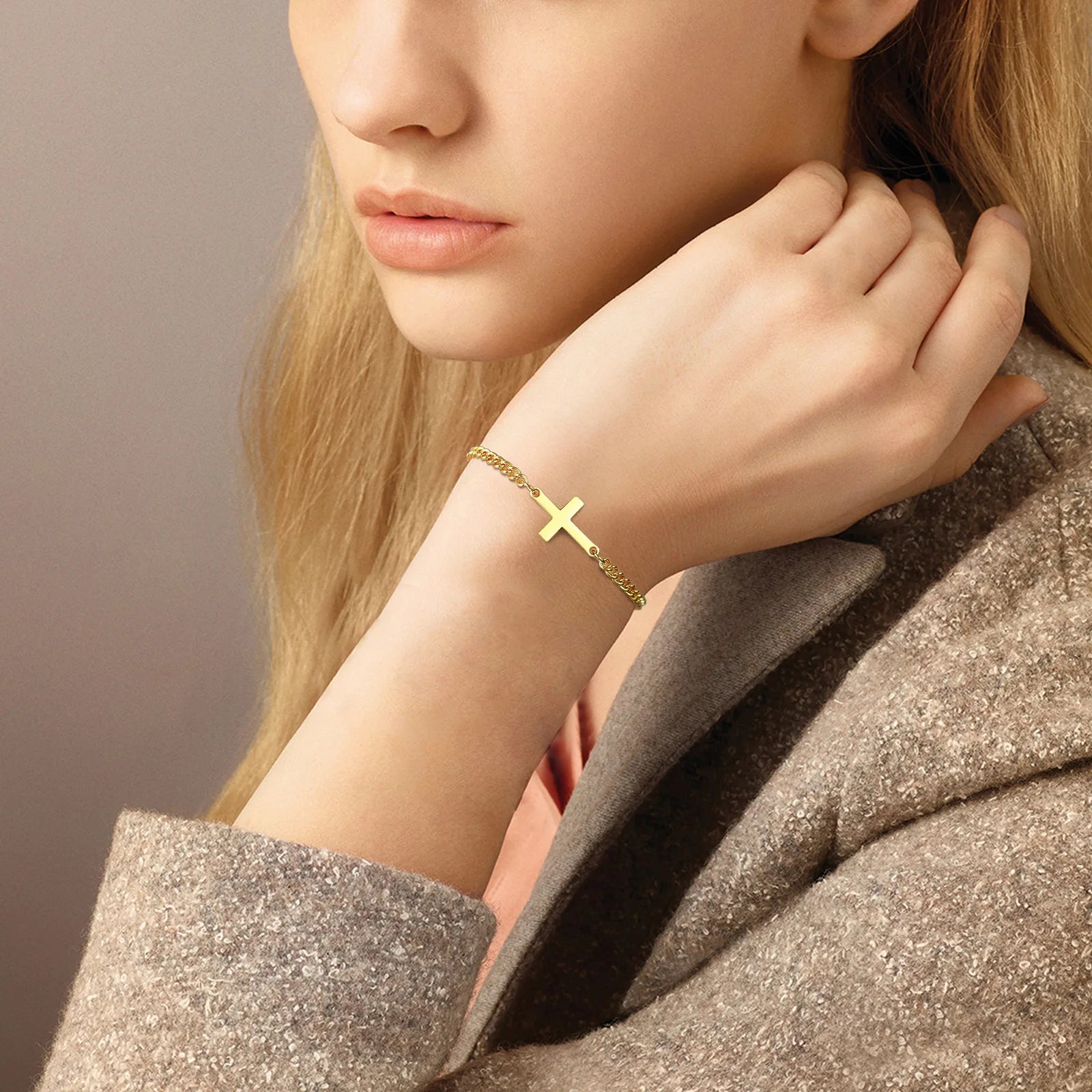 Close-up of a person wearing a gold bracelet with a cross design on a neutral background