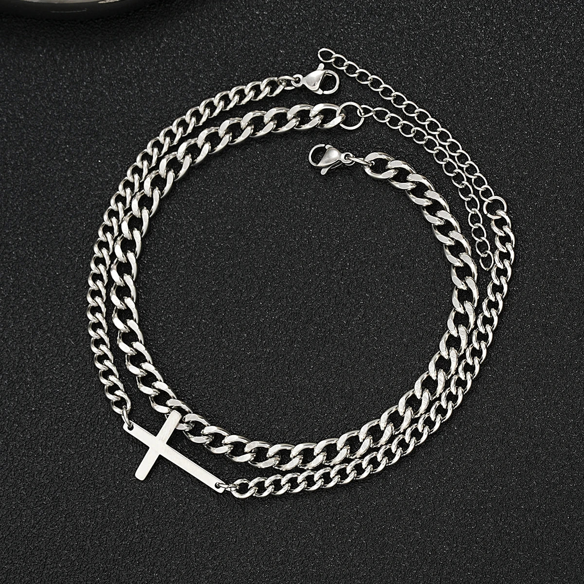 Silver chain bracelet with a cross charm on a black background