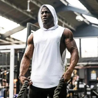 Man in a white tank top and hoodie holding ropes in a gym setting