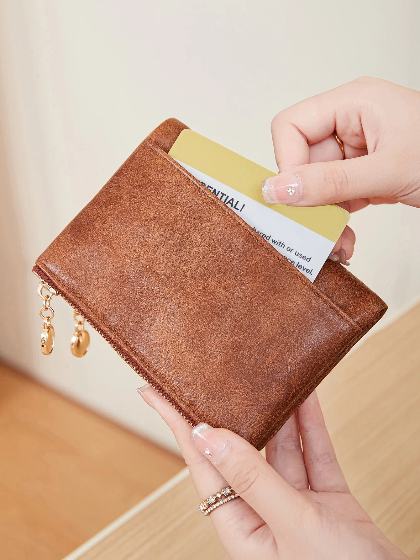 Brown wallet with gold zipper pulls held by a hand against a neutral background