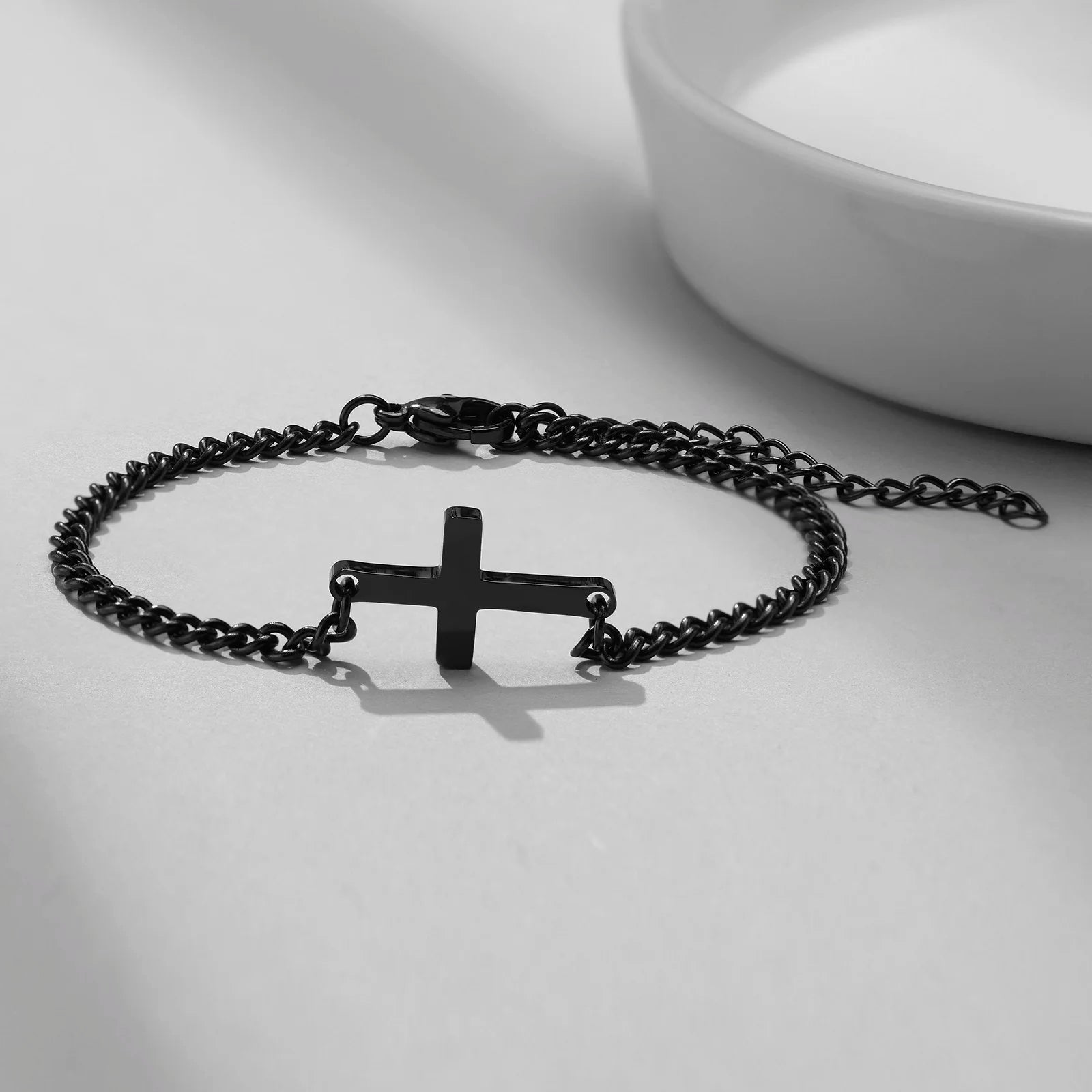 Black chain bracelet with a cross pendant on a light gray background