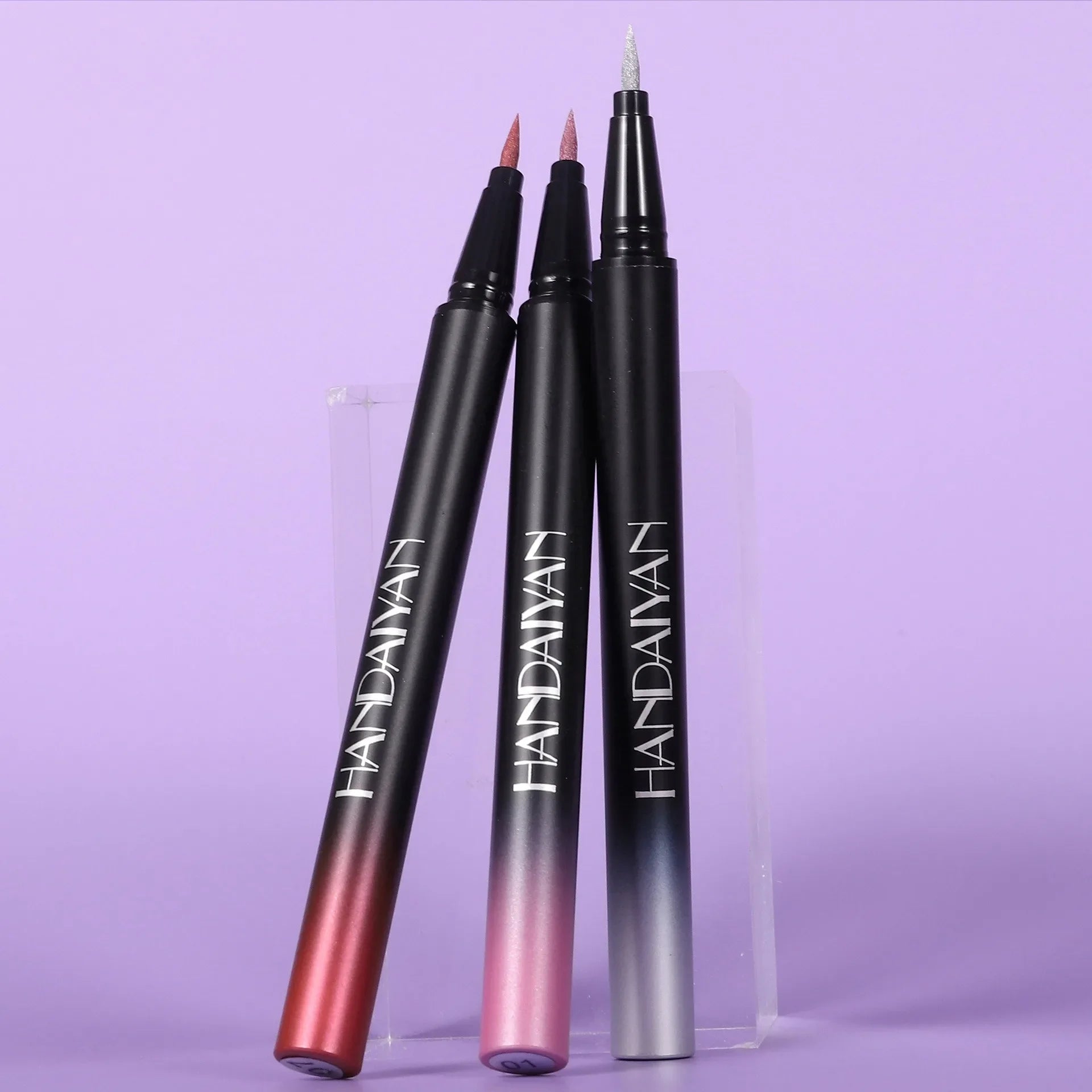 Three black lip liner pens with gradient colors on a purple background, featuring the brand 'HANDAVAN'.